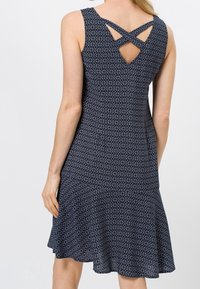 Marineblaues ärmelloses Kleid mit geometrischem Muster, ausgestelltem Saum und gekreuzten Trägern am Rücken. Hergestellt aus leichtem Stoff.