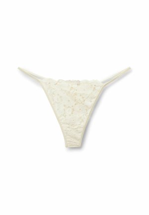 Tanga en dentelle ivoire avec motif floral et fines doubles bretelles latérales sur fond blanc.