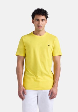 T-shirt gialla in cotone con scollo rotondo, maniche corte e un piccolo logo nero sul petto a sinistra; texture liscia e design aderente.