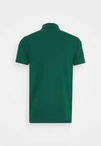 Polo vert en coton avec manches courtes et col classique. Texture lisse, lignes épurées, sans motifs ni logos visibles.