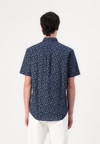 Chemise à manches courtes bleu marine avec un motif cachemire, dotée d'un col boutonné et d'un ourlet arrondi. Le tissu semble lisse et léger.