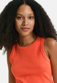 Oranges Ripptanktop mit Rundhalsausschnitt und breiten Schulterträgern. Der Stoff ist glatt mit leichtem Stretch.