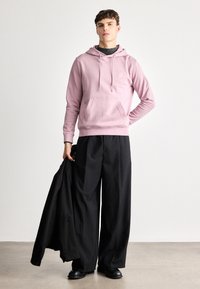 Roosa kapuutsi tõmblukuga ja esikotiga,  koos laia musta pükstega. Mudel hoiab musta jakk. Sile tekstuur, juhuslik disain.