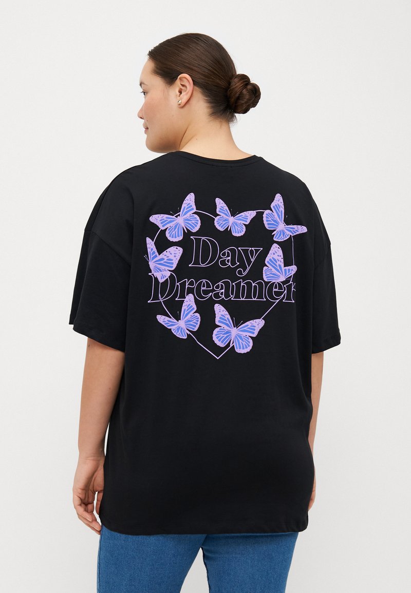 Camiseta oversized negra con gráficos de mariposas moradas y el texto "Day Dreamer" dentro de una forma de corazón en la parte trasera. Material de algodón.