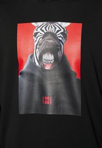 Camiseta negra con un estampado gráfico de una cebra con dientes prominentes sobre un fondo rojo. El logotipo dice "HUGO" en la parte inferior.