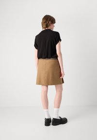 Schwarze kurzärmlige Bluse, die mit einem braunen A-Linien-Rock kombiniert ist, der einen Leopardenmuster-Taillenbund hat. Das Model trägt schwarze Plateauschuhe und weiße Socken.