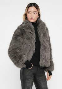 Grå faux fur jakke med en fluffy tekstur, cropped design og bred krave. Stylet over en sort top og parret med mørke bukser.
