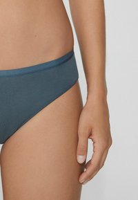 Tmavě modré bikini spodní díl s hladkou texturou, širokým pasem a nízkým střihem. Materiál vypadá měkký a elastický.