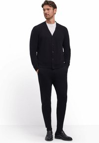 Cardigan nero con scollo a V, sei bottoni, polsini a coste, abbinato a pantaloni neri a sigaretta e scarpe nere, realizzato in un tessuto texturizzato.
