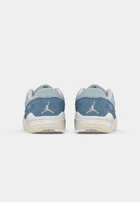 Baskets en denim bleu avec une semelle en caoutchouc blanc, présentant un logo au niveau du talon et des accents texturés sur le matériau supérieur.