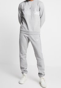 Grå sweatshirt och sweatpants set gjort av bomullsblandat tyg. Har vitt logo, ränder och ribbade mudd. Atletisk passform och mjuk textur.