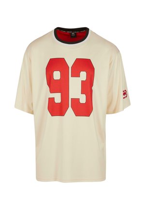 T-shirt crème à manches courtes avec un grand graphique rouge "93" sur le devant et un détail de col noir et rouge. Texture de tissu douce.