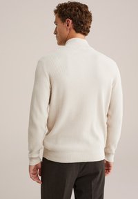 Pulover crem cu model rubricat, cu guler înalt și mâneci lungi, având un finisaj texturat. Pur tată cu pantaloni închiși, croiți.