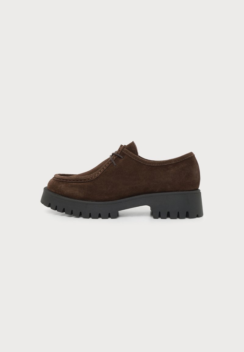 Chaussure à lacets en suède marron foncé avec semelle épaisse en caoutchouc noir à crampons, talon bas et épais, et bout arrondi, vue de côté sur fond blanc.