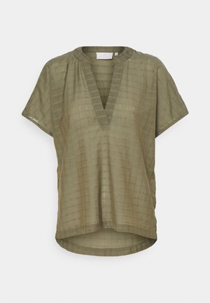 Blouse ample à manches courtes vert olive avec une texture subtile à carreaux, col en V profond, ourlet asymétrique et coupe décontractée.