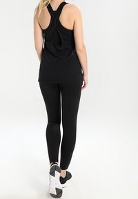 Black athletic tank top with a racerback design and cut-out detail at the back, paired with black leggings and black athletic shoes.
