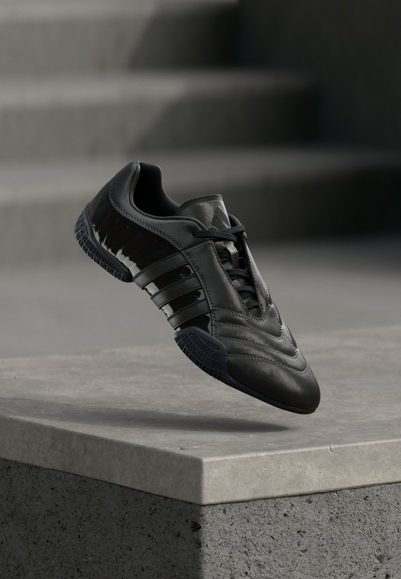 Svart sportsko med glatt skinn, tre reflekterende striper, teksturert detaljering på sålen og en slank, avrundet silhuett.