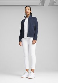 Tumesinine tõmblukuga jakk, valge polo, valged slim-fit püksid ja valged spordijalatse. Sile kangas kaasaegse lõikega, ilma nähtavate mustrite või aktsentideta.
