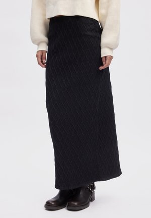 Black maxi skirt with a diamond pattern. Made of textured fabric, featuring a fitted waist and a straight silhouette. Worn with ankle boots.
