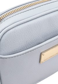 Lichtblauw leren tasje met een textuur, gouden rits en een rechthoekig hardware accent in goudkleur aan één kant.