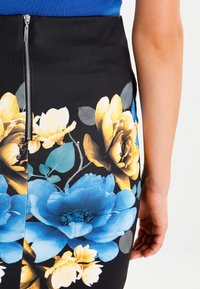 Gonna a matita floreale con grandi fiori blu e gialli su sfondo nero, con una cerniera argentata visibile sul retro.