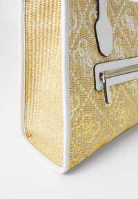 Woven straw handbag in light yellow with white trim. Features embroidered logo pattern and a zippered pocket on the front for added detail.