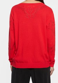 Suéter de punto rojo con un ajuste holgado, cuello redondo y elaboradas decoraciones de strass en la espalda y las mangas.