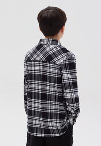 Camisa de cuadro blanco y negro hecha de franela, con cuello abotonado, mangas largas y dobladillo curvado.