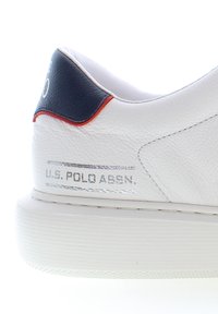 Sneaker bianca in pelle con una finitura texture, dotata di un inserto sul tallone blu navy e rosso e un marchio in metallo argentato sul lato. Suola in gomma.