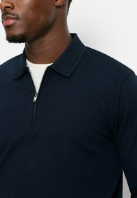 Marineblauwe rits polo met kraag, voorzien van een zilveren rits en een soepele textuur. Gemaakt van lichtgewicht materiaal, geschikt voor lagen.