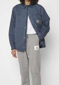 Blå kviltad jacka med tryckknappar och två bröstfickor, bärs över en vit t-shirt och grå sweatpants med en logotyplapp.