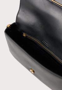 Μαύρη δερμάτινη τσάντα με λεία υφή, η οποία διαθέτει χρυσό φερμουάρ και μεταλλικά στοιχεία. Το εσωτερικό περιλαμβάνει μία τσέπη με φερμουάρ για ασφαλή αποθήκευση.