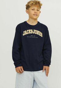 Tamsiai mėlynas džinsinis ilgomis rankovėmis marškinėliai, pagaminti iš medvilnės, su geltonu ir baltu "JACK & JONES" logotipu. Laisvas modelis su gumuotomis rankogaliais ir apykakle.