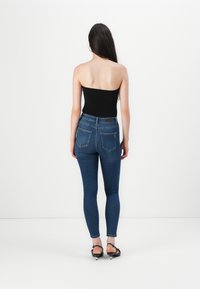 Svart axelbandslös topp i kombination med åtsittande blå jeans; bakview visar slät tyg och femficksdesign, med en ren och skräddarsydd passform.