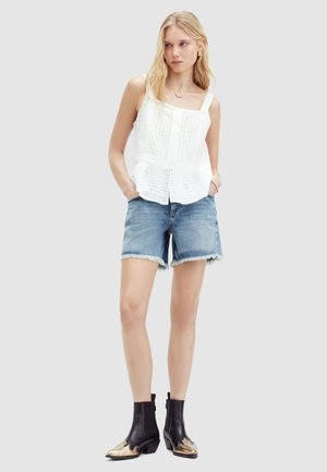 Top peplum blanco bordado con tirantes ajustables, combinado con pantalones cortos de mezclilla azul. Botines negros con acentos metálicos.