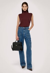 Bordó tílko bez rukávů s vysokým límcem; modré široké džíny cargo s kapsami; černá taška s texturovaným povrchem; lodičky na podpatku.