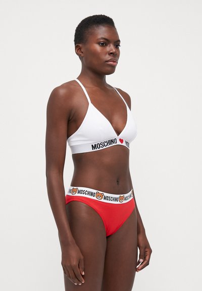 Fehér bikini felső vékony pántokkal és fekete márkázott csíkkal; piros bikini alsó fehér csíkkal, amelyen egy medve logó és szöveg található.