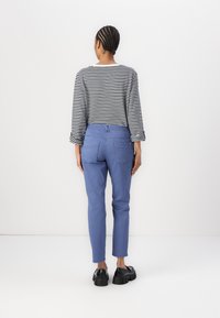 Blue slim-fit pants with a mid-rise waist paired with a black and white striped long-sleeve shirt, view from the back.