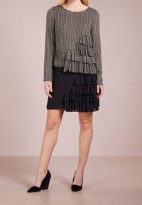 Czarna i biała wzorzysta bluzka z długimi rękawami i falbanami z przodu, zestawiona z czarną spódnicą z falbanami. Całość dopełniają czarne szpilki.
