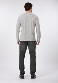 Μακρυμάνικο γκρι πουκάμισο με ρίγες, στρογγυλή λαιμόκοψη, συνδυασμένο με σκούρο γκρι παντελόνι και μαύρα αθλητικά παπούτσια. Το πουκάμισο έχει λεπτή υφή και εφαρμοστή γραμμή.