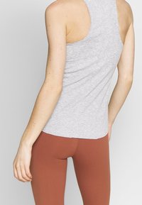 Canotta grigia senza maniche con scollatura arrotondata e texture liscia. Abbinata a leggings aderenti color ruggine.