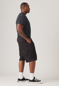 Svarte cargo shorts med avslappet passform, med sidelommer og glatt stoff. Kombinert med en mørkegrå t-skjorte med kort erm og svarte joggesko.