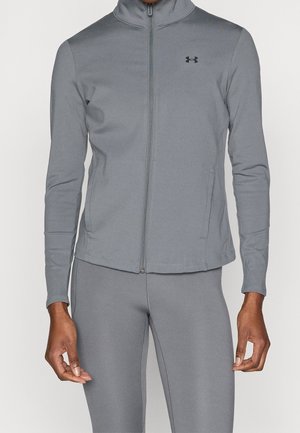 Person iført en grå atletisk jakke med fuld lynlås og matchende leggings med et lille sort Under Armour-logo på brystet.