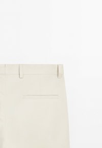 Beige trousers with belt loops and a single back welt pocket on a plain white background.
