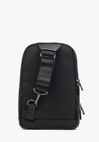Černý messenger batoh s hladkým nylonovým povrchem a koženými detaily. Má nastavitelný popruh a stříbrné kovové doplňky. Dvě zipové kapsy.