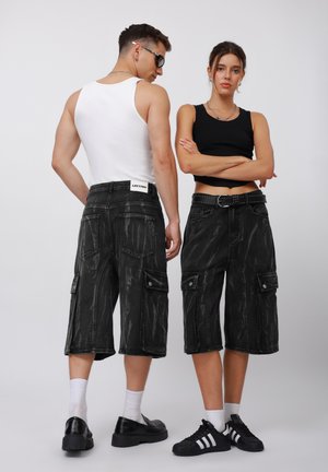 Shorts cargo en denim noir avec une texture délavée, de grandes poches et un design stylisé. Portés avec des hauts simples et des baskets.