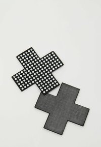 Dva černé záplaty ve tvaru kříže na bílém povrchu, jedna zdobená malými průhlednými kamínky, druhá jednobarevná s matným povrchem.