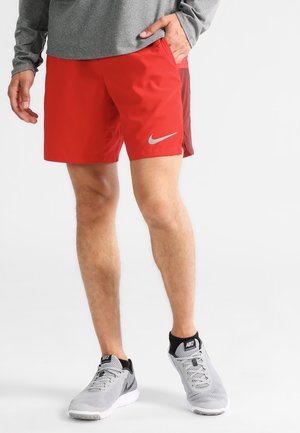 Shorts de sport légers rouges et marron avec poches latérales et un logo Nike argenté. Associés à des baskets en mesh grises avec des accents noirs.