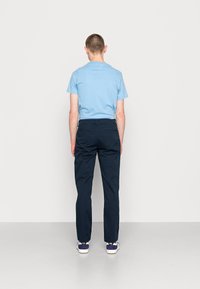 Hellblaues Kurzarmhemd, marineblaue Hose und weiße Sneaker mit dunklen Akzenten, von hinten vor einem schlichten Hintergrund betrachtet.