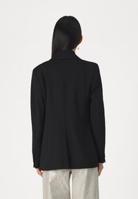 Black tailored blazer featuring a notched collar, structured shoulders, and subtle stitching details, paired with shiny, textured silver pants.